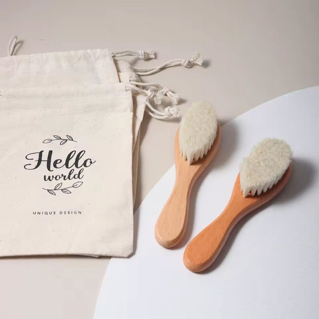 Zwei Pinsel mit Holzstiel und weißen Borsten liegen neben einem beigen Spielzeugbeutel "Hello World" (14,5x23,5cm) von Hello World - perfekt als Geschenk zur Geburt - auf einer hellen Fläche.