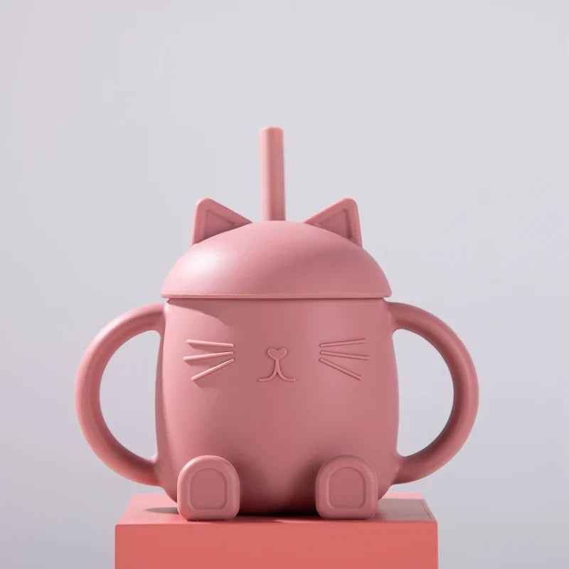 Der Hello World Trinkbecher Katze sitzend Pink [13x11cm] ist ein rosafarbener Becher in Form einer Katze mit einem Deckel mit Katzenohren, einem Strohhalm, zwei armförmigen Henkeln und pfotenförmigen Füßen, der vor einem schlichten hellen Hintergrund abgebildet ist.