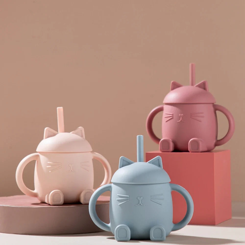 Drei Hello World Trinkbecher Katze sitzend Rosa [13x11cm] mit Katzenohren-Deckel, Strohhalm, Schnurrbart-Details und Henkel werden auf einer beigen Oberfläche mit passenden Blöcken in Pastellrosa, Mauve und Blau präsentiert.