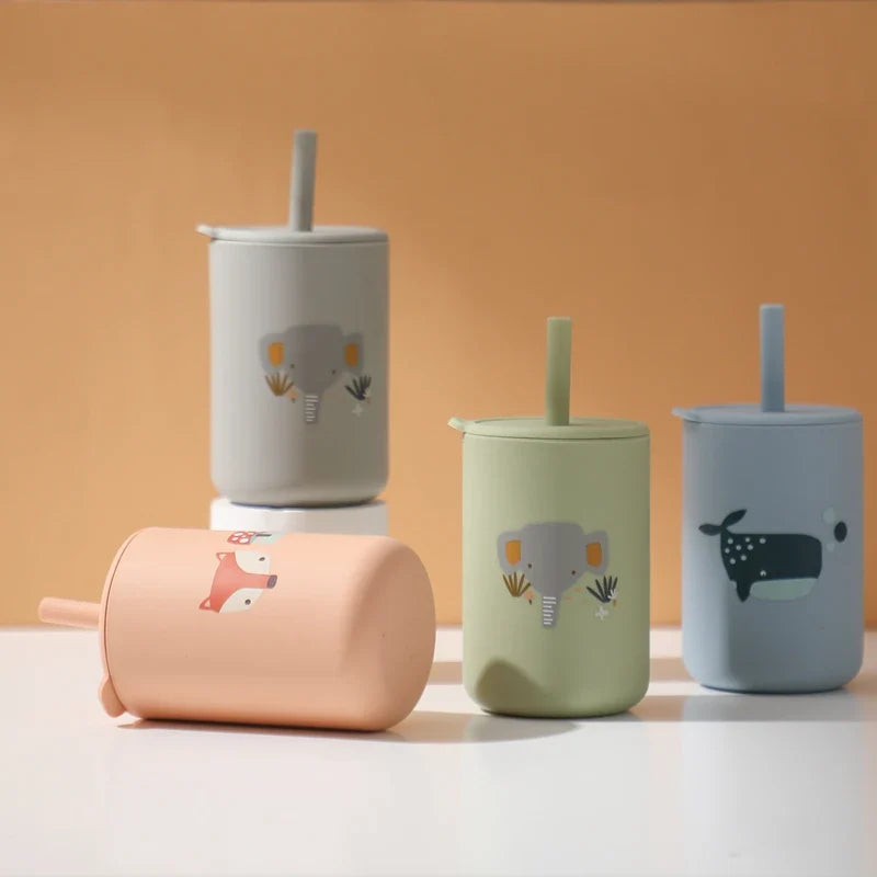 Vier Hello World Trinkbecher mit Motiv Grün [6x12,5cm] mit Tiermotiven sind auf einer hellen Fläche vor einem beigen Hintergrund abgebildet; drei stehen aufrecht und ein BPA-freier Pfirsichbecher mit Elefantenmotiv liegt hin.