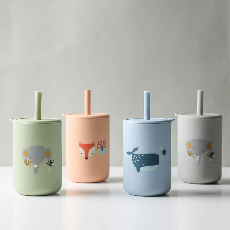 Vier grüne Hello World Trinkbecher mit Motiv (6x12,5 cm), aus BPA-freiem Silikon, jeweils mit Deckel und Strohhalm. Die Becher zeigen Elefanten- und andere Tierdesigns und sind vor schlichtem Hintergrund angeordnet.