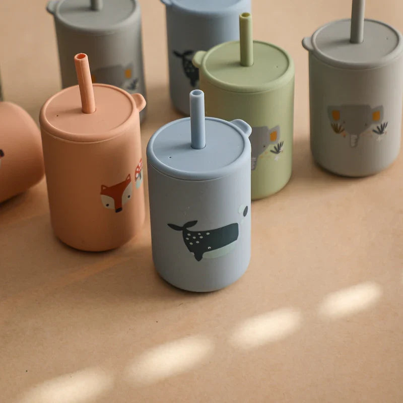 Ein Set von Hello World Trinkbechern mit Motiv Orange [6x12,5cm], BPA-frei, in Pastellfarben mit Deckeln, Strohhalmen und niedlichen Wal-, Fuchs- und Elefantenmotiven, ausgestellt auf einer hellbraunen Oberfläche unter sanfter Beleuchtung.