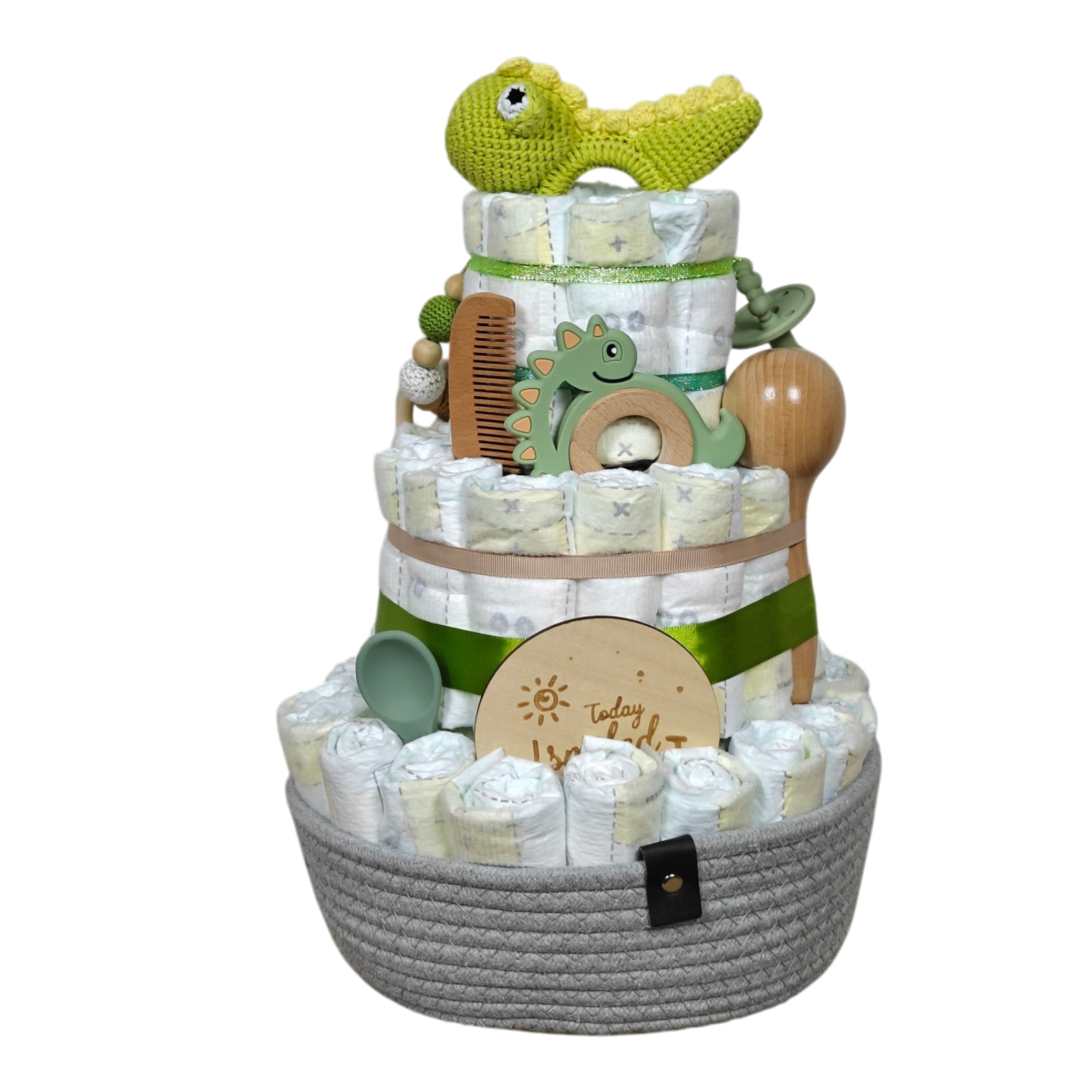 Die Hello World Windeltorte Dino [25x38cm] besteht aus drei Etagen, grünen und beigen Bändern und Babyutensilien: gehäkelter Dinosaurier, Holzkamm, Bürste, Beißring, Schnullerclip, Silikonlöffel und Meilensteinmarker - das perfekte Geschenk zur Geburt!.