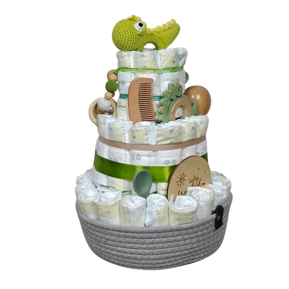 Die Hello World Windeltorte Dino [25x38cm], eine dreistöckige Windeltorte mit grünem Band, Holzspielzeug und einem gehäkelten Alligator als Topper in einem grauen Korb, ist ein bezauberndes Geschenk zur Geburt voll Baby-Essentials.