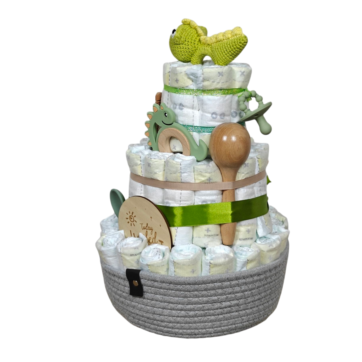 Die Windeltorte Dino [25x38cm] von Hello World besteht aus drei Etagen, grünen Bändern, einem gehäkelten gelben Dino, einem Dino-Holzspielzeug, einem Löffel und einem grauen Korb - vollgepackt mit Baby-Essentials ist sie das perfekte Geschenk zur Geburt.