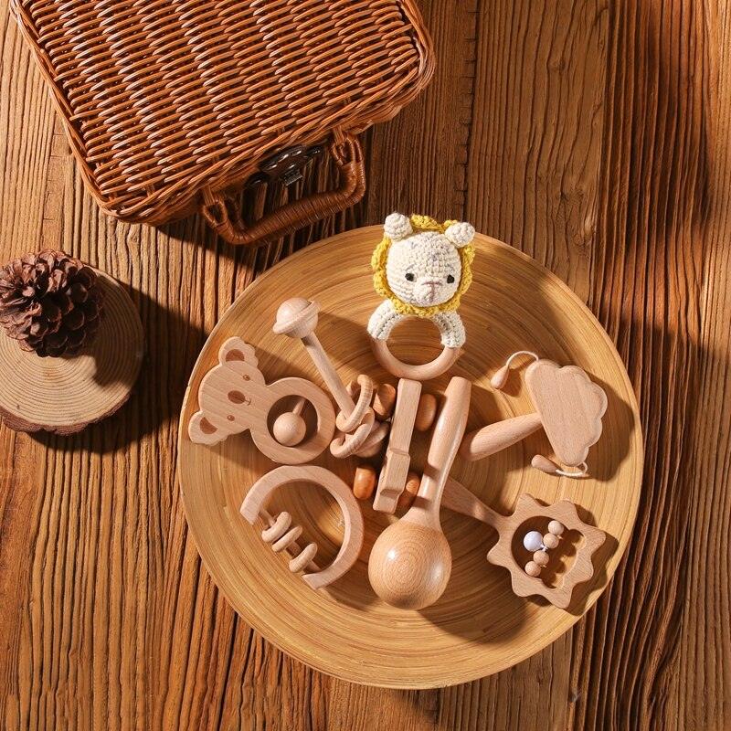 Auf einem runden Holzteller liegt diverses Hello World Holzspielzeug aus dem Xenia Baby Geschenk zur Geburt Set, mit tierischen Rasseln und einem gehäkelten Löwenring - ideal für die sensorische Entwicklung.