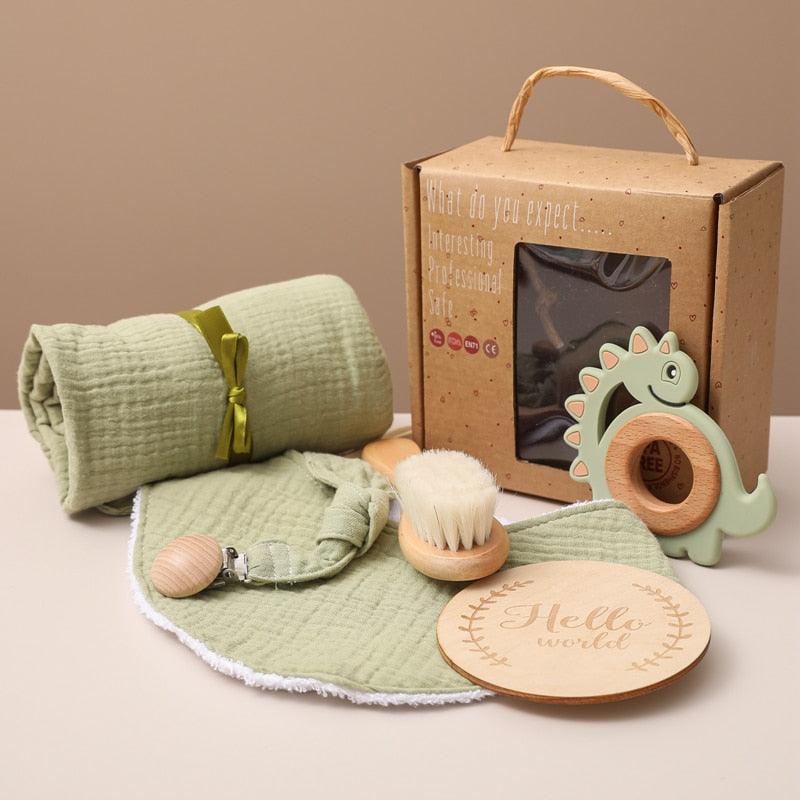 Das Yoshi Baby Geschenk zur Geburt von Hello World enthält eine weiche grüne Decke, ein passendes Lätzchen, eine Schnullerklemme, eine Haarbürste aus Holz, einen Dinosaurier-Beißring aus Silikon und eine Plakette mit dem Schriftzug "Hello World", alles in einer braunen Schachtel.