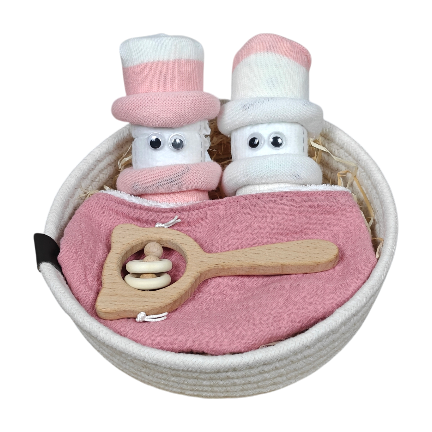 Ein weißes Körbchen enthält zwei puppenhaft gerollte weiße Handtücher mit rosafarbenen Mützen und Kulleraugen, ein rosafarbenes Tuch und eine hölzerne Babyrassel - ein bezauberndes Kuschelkörbchen-Blütenzwillinge-Babygeschenkset von Hello World.