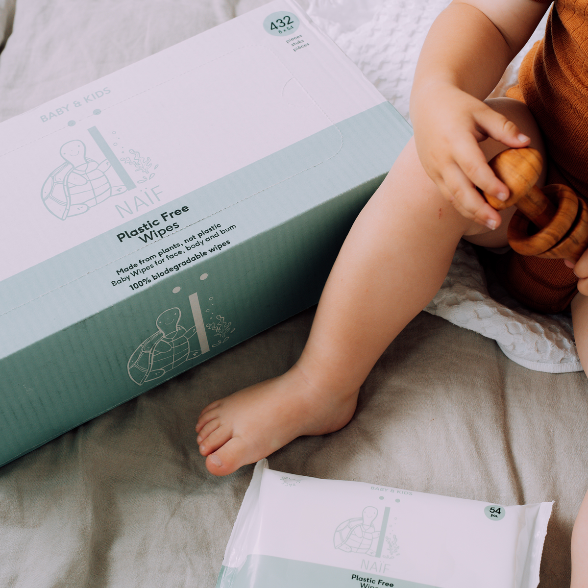 Naïf supply pack of plastic-free baby wipes and opened individual pack next to a toddler.