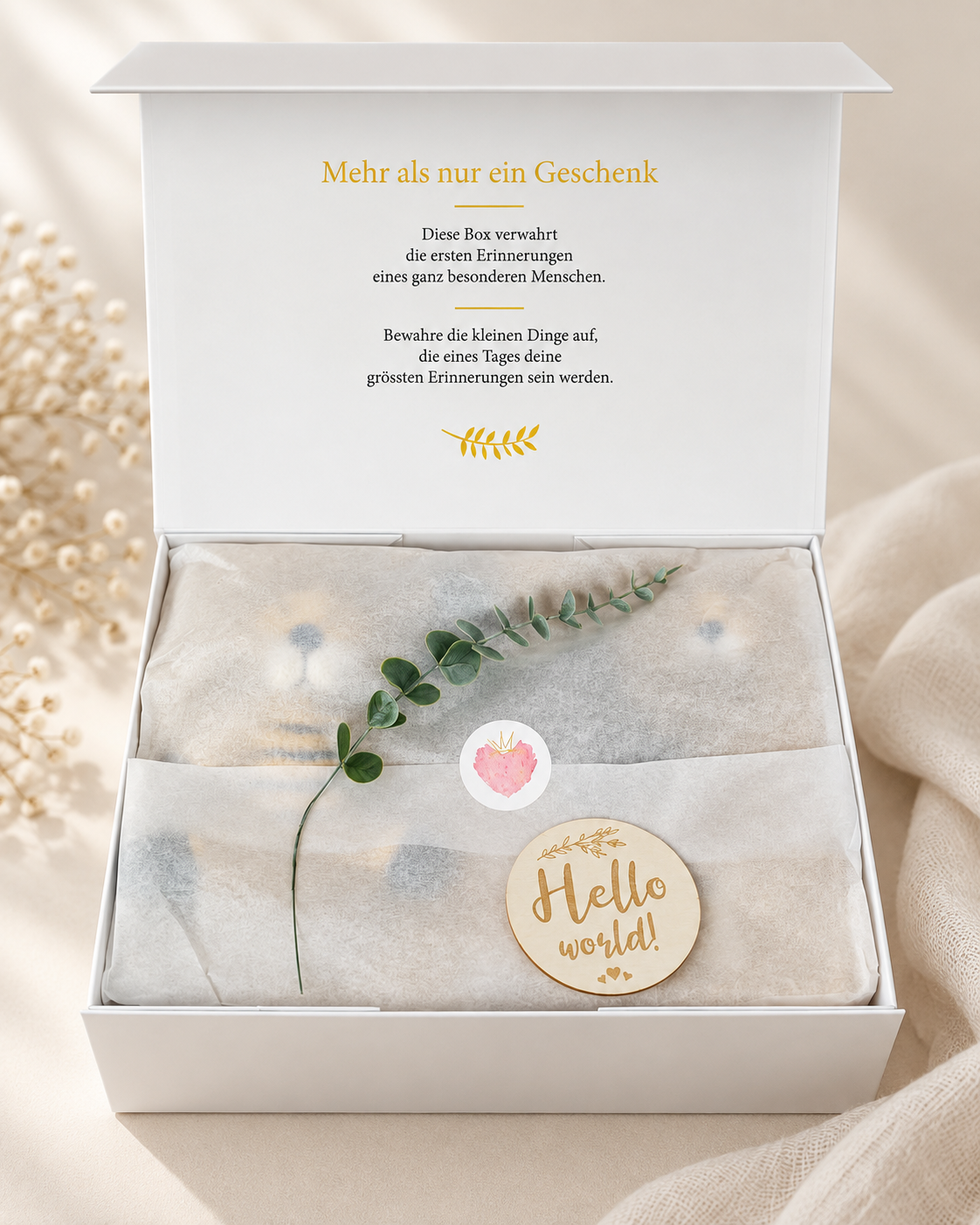 Geöffnete Premium Geschenkbox zur Geburt mit Seidenpapier, Eukalyptuszweig, Hello World Holzanhänger und Erinnerungsbotschaft im Deckel.