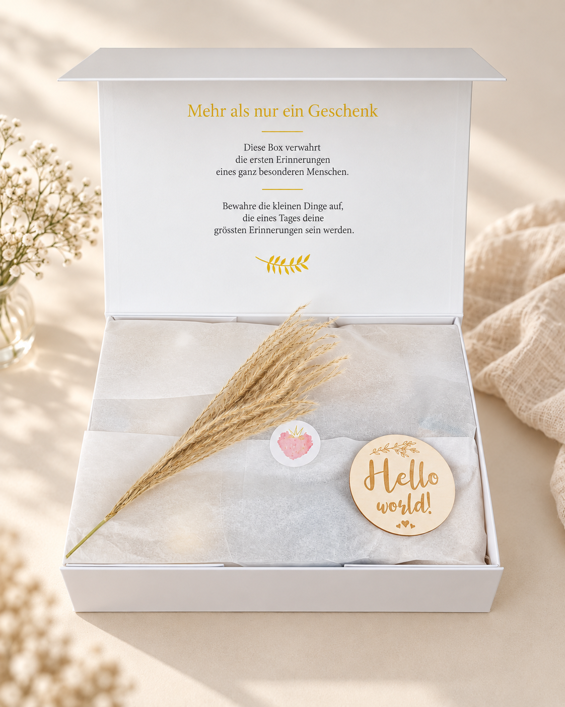 Geöffnete cremeweisse Premium Geschenkbox mit Erinnerungsaufdruck im Innendeckel, Seidenpapier, Trockenblume und rundem Hello World Holzanhänger.