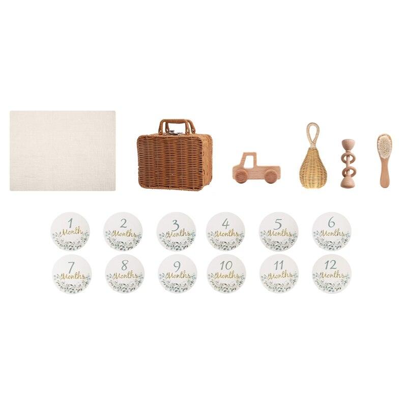 The Hello World Rusty Baby birth gift includes baby milestone cards (1-12 months), a beige cloth, a small wicker suitcase, a wooden toy truck and a stacking toy, a rattan rattle and a wooden hairbrush.