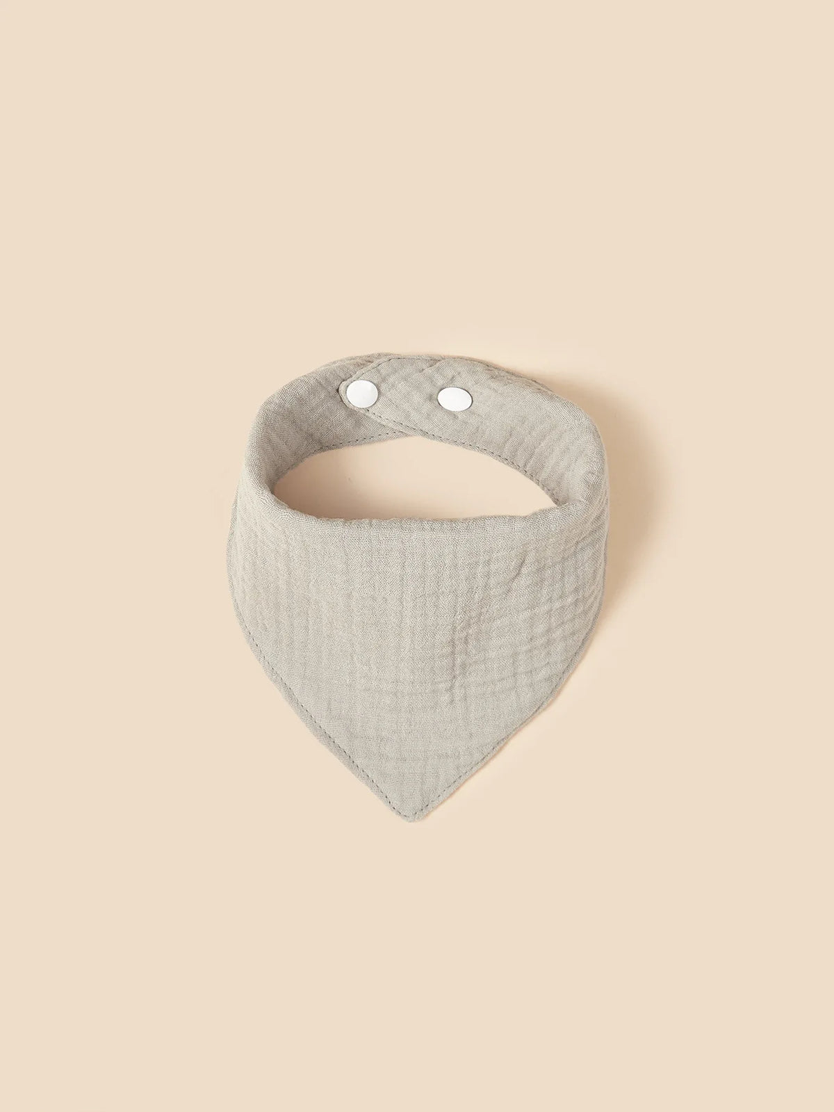 Un morbido bavaglino a bandana in cotone grigio Hello World con due bottoni a pressione bianchi è piatto su uno sfondo beige a tinta unita.