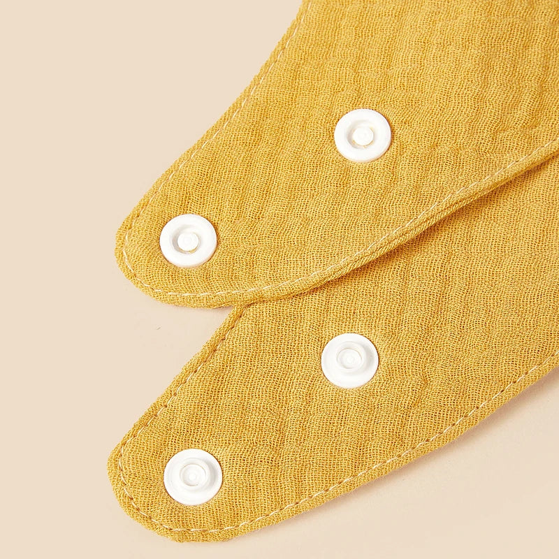 Primo piano di due bavaglini Hello World in cotone giallo sovrapposti con bottoni automatici bianchi su sfondo beige.