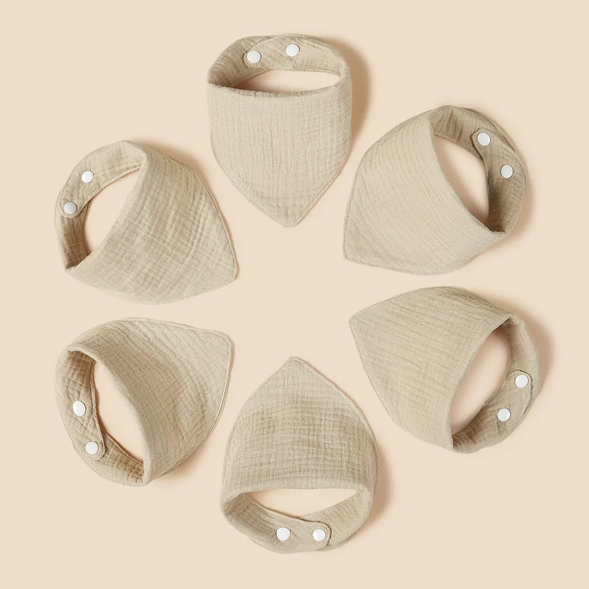 The six "Cotton Khaki Bibs" from Hello World are arranged in a circle on a light brown background. Each bib has two visible white snaps and a khaki textured cotton design.