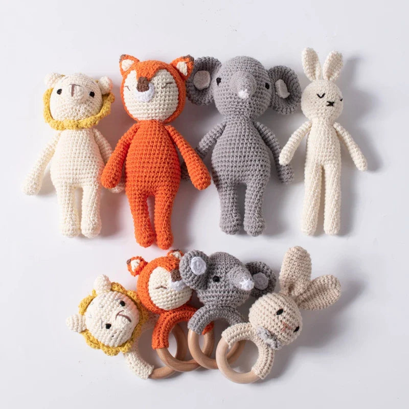 Quattro bambole di animali Hello World all'uncinetto (incluso il leone lavorato a maglia, 18,5 x 10 cm) sono disposte sopra quattro sonagli per neonati ad anello in legno abbinati con le stesse facce di animali, il tutto su uno sfondo bianco.