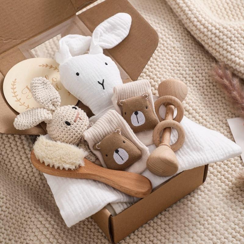 Das Whitii Baby Geschenk zur Geburt von Hello World besteht aus einem weichen weißen Schnuffelhasen, einer gestrickten Rasselhase-Rassel, Bärensocken, einer hölzernen Haarbürste und zwei hölzernen Rasseln auf einer cremefarbenen Strickdecke - eine bezaubernde Geschenkbox für Neugeborene.