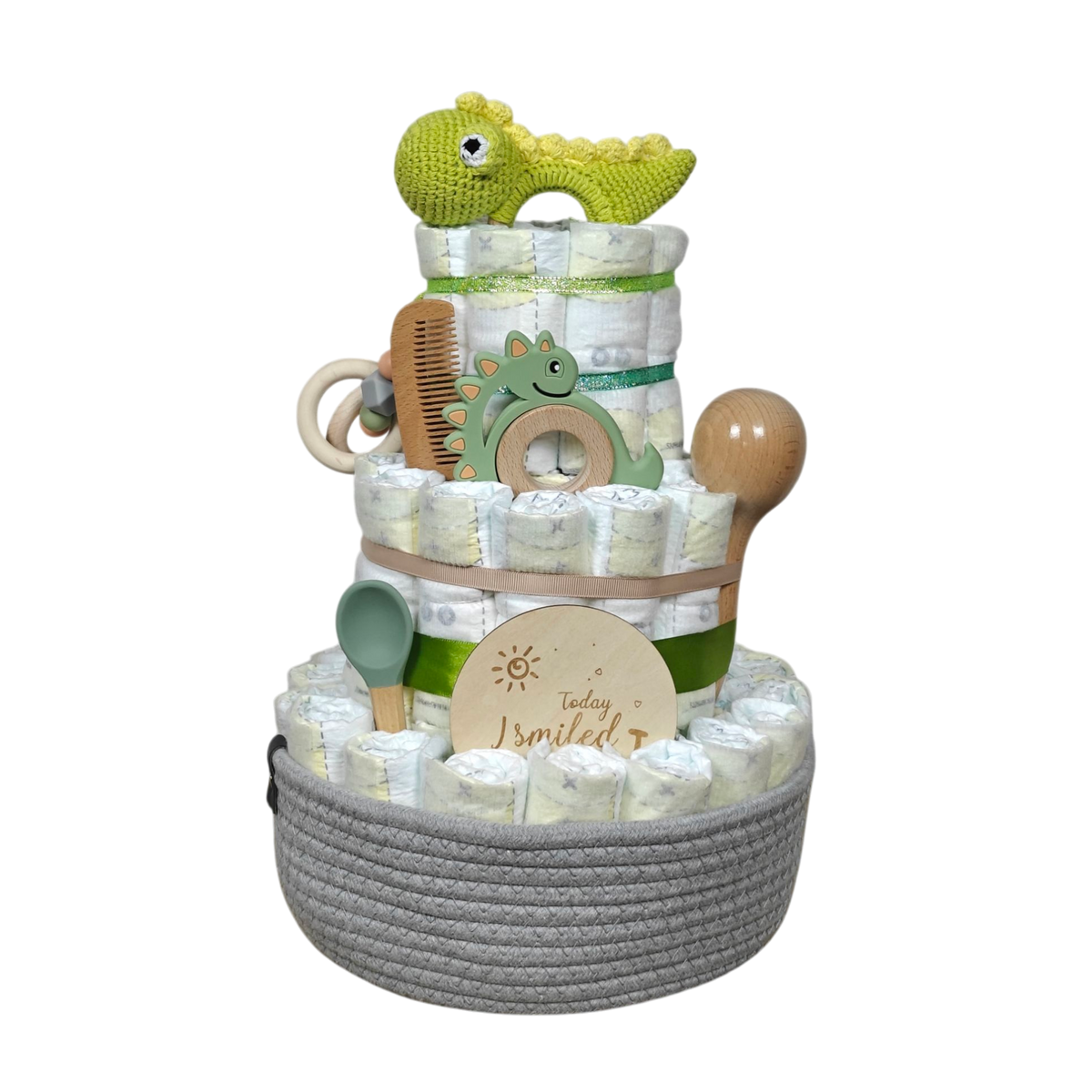 Die Windeltorte Dino [25x38cm] von Hello World besteht aus drei Etagen, dekoriert mit Windeln, grünem Häkel-Dino, Holzkamm, Rassel und "Today I smiled"-Schild, schön präsentiert im grauen Korb - das ideale Geschenk zur Geburt.