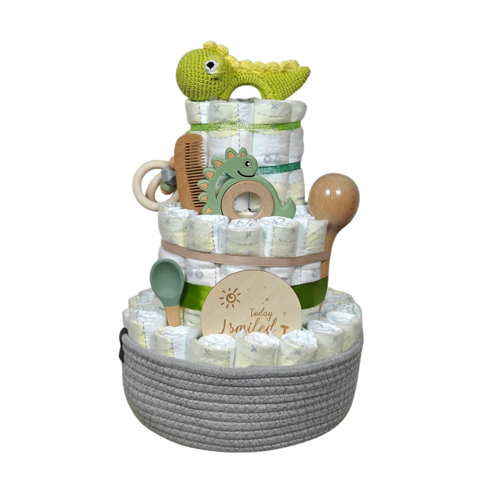 Die Windeltorte Dino [25x38cm] von Hello World besteht aus drei Etagen, dekoriert mit Windeln, grünem Häkel-Dino, Holzkamm, Rassel und "Today I smiled"-Schild, schön präsentiert im grauen Korb - das ideale Geschenk zur Geburt.