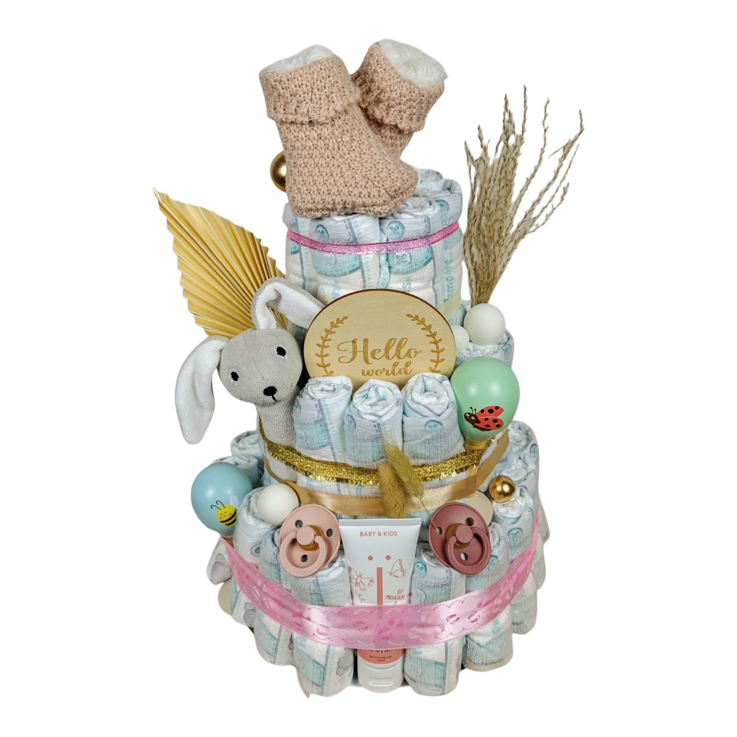 Vue latérale du gâteau de couches Elaia avec hochet lapin, tétines BIBS, crème de soin NAÏF et jolis détails roses et naturels