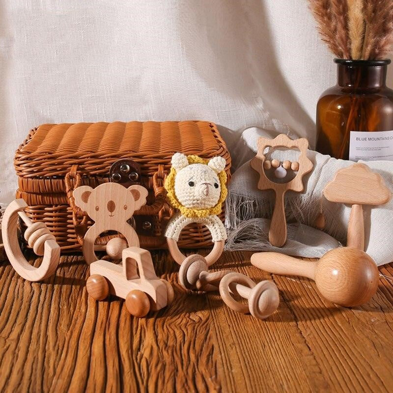 Le cadeau de naissance Xenia Baby de Hello World contient des jouets en bois faits à la main tels qu'une voiture, des anneaux de hochet et un lion avec une crinière crochetée - joliment disposés sur du bois, idéaux pour le développement sensoriel de bébé.